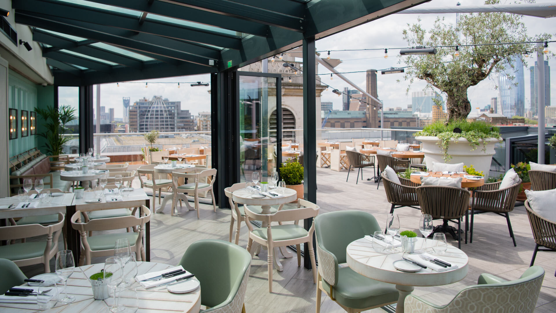 11 Rooftop Bars & Restaurants in the City of London - Vintry & Mercer Hotel 11 Rooftop Bars & Restaurants in the City of London - Vintry & Mercer Hotel - circular tables on roof terrace, large potted olive tree
