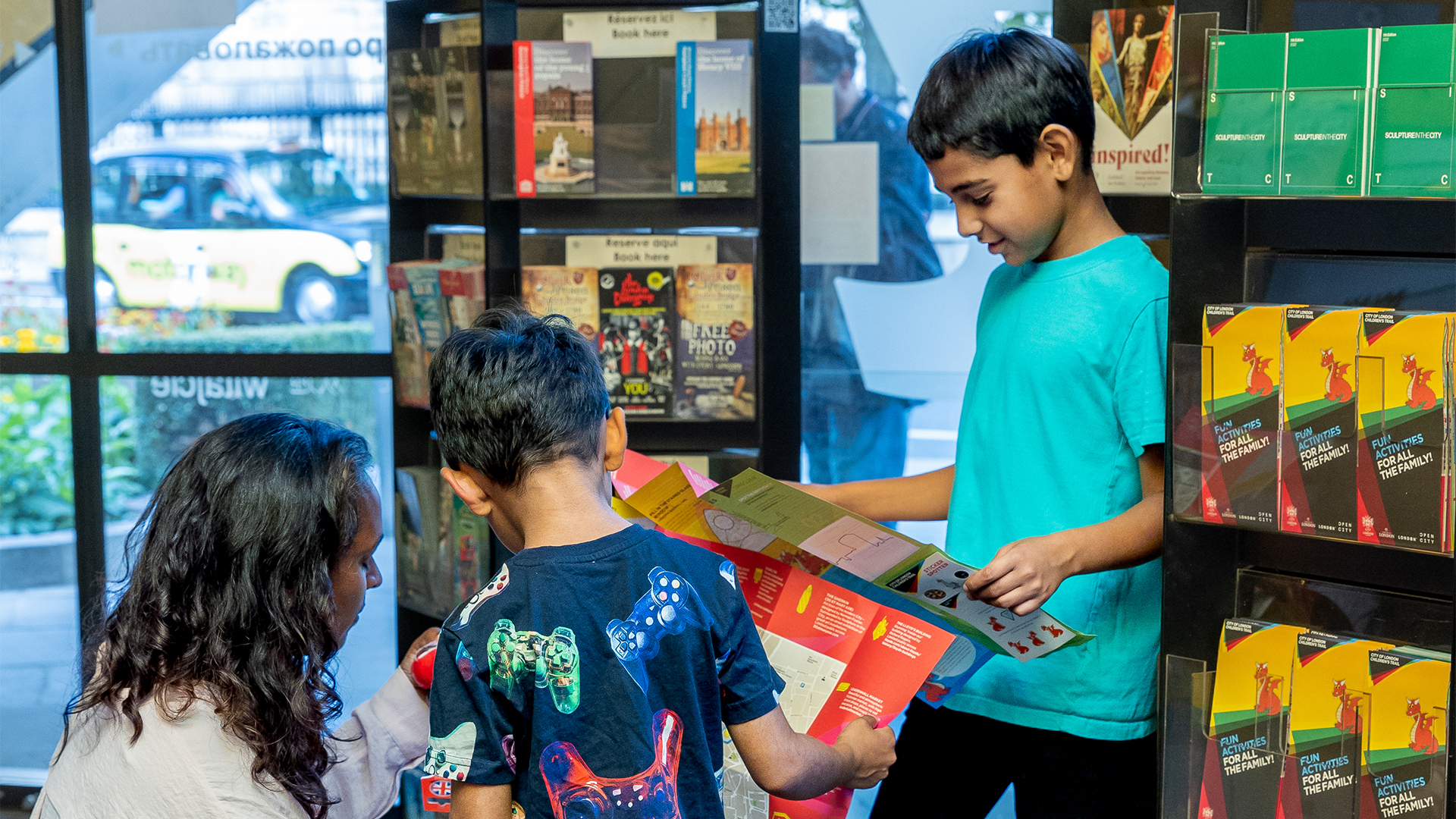 Two children with their mum looking at a map at an information centre with flyers on racks in the background.
