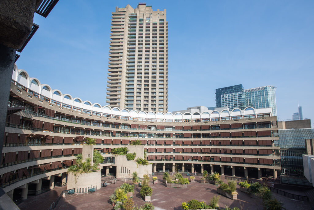 Barbican Architecture Tours - large curved building housing flats and a arching rooftops - view of a barbican highrise in the distance
