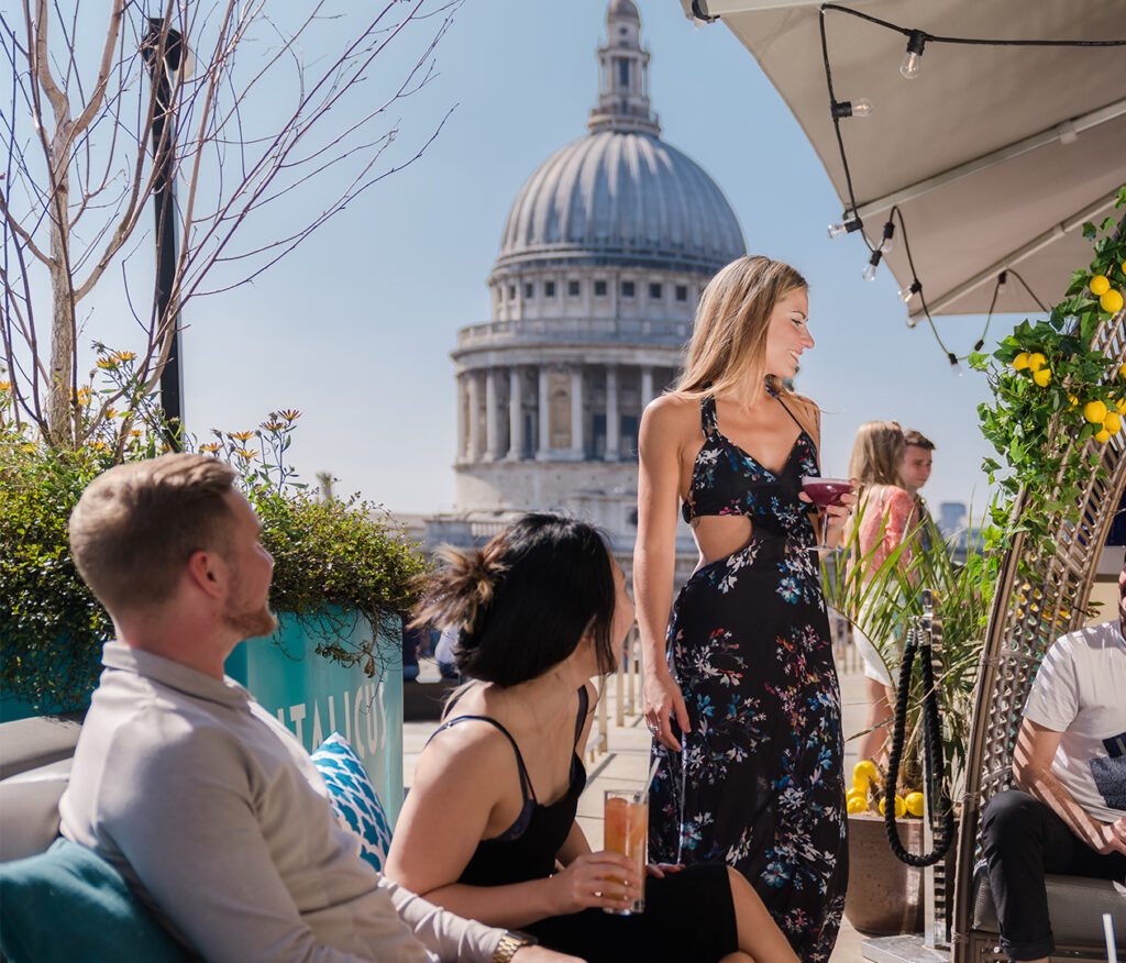 11 Rooftop Bars & Restaurants in the City of London - Madison at One New Change Group of friends having a drink at a rooftop terrace with St Paul's cathedral dome in the background