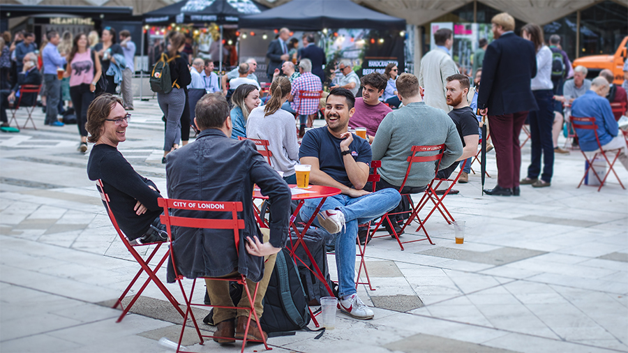 People sitting on red chairs outdoors with food stalls behind