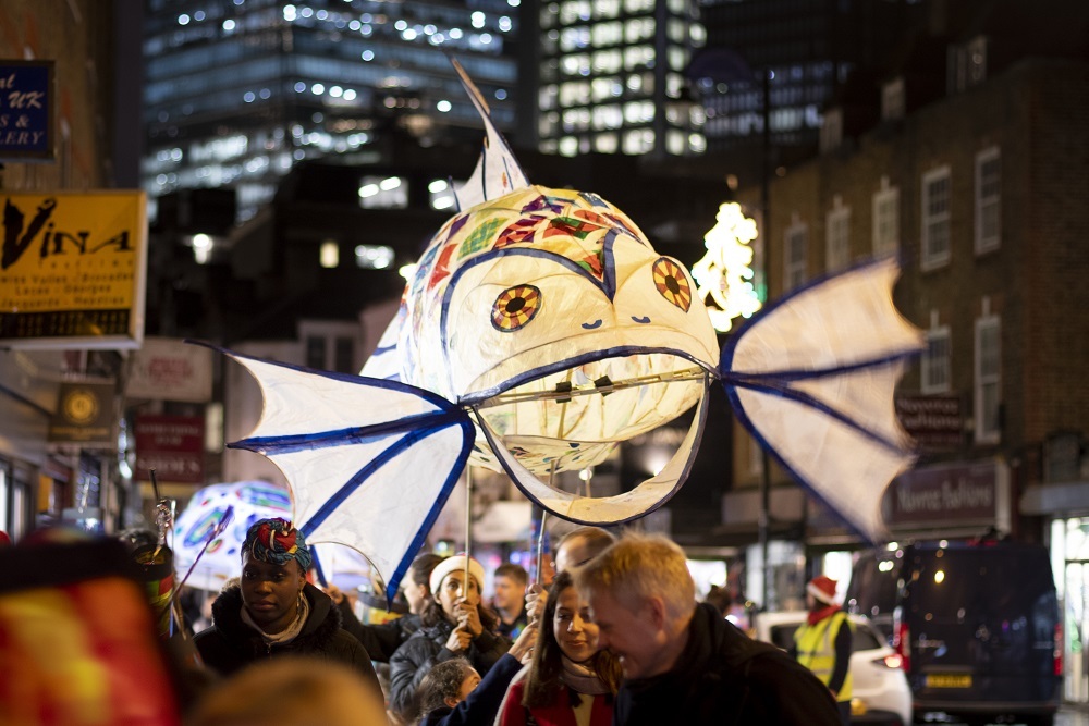 Illuminated lantern in the form of a fish being carried by people on the street