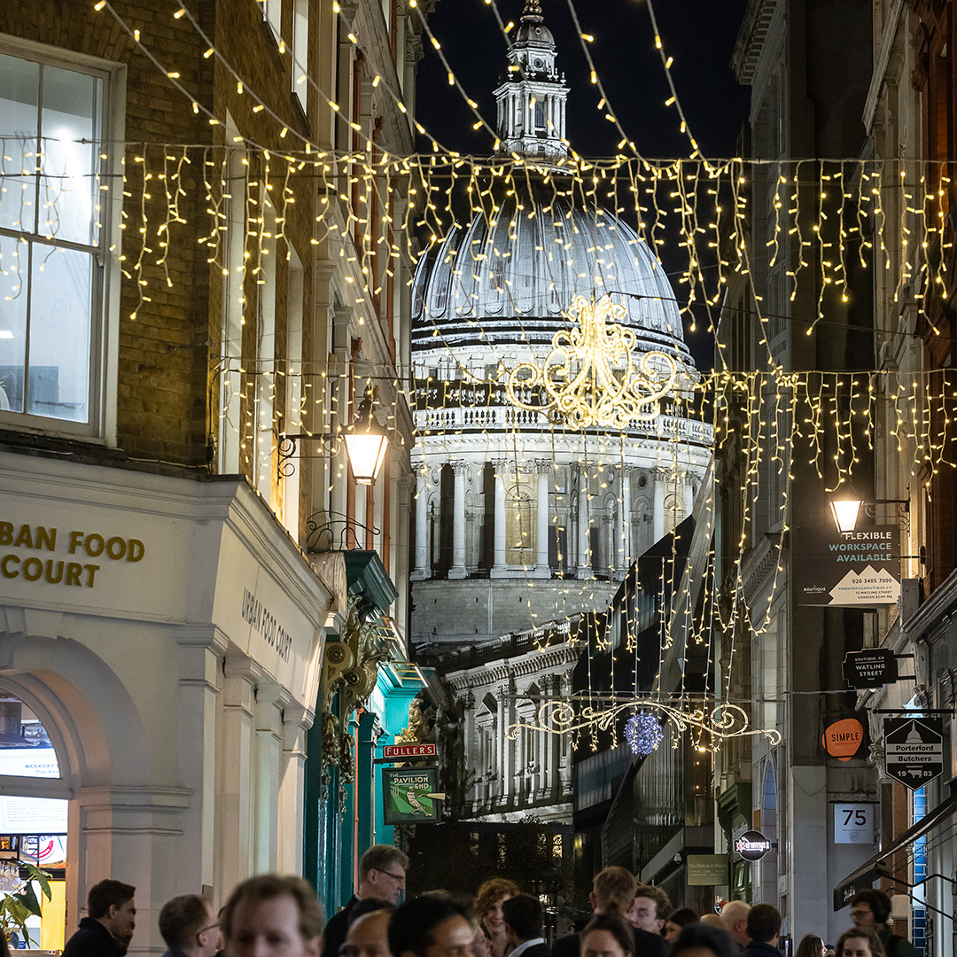 Narrow street decorated with Christmas lights and a view of St Paul's Cathedral dome