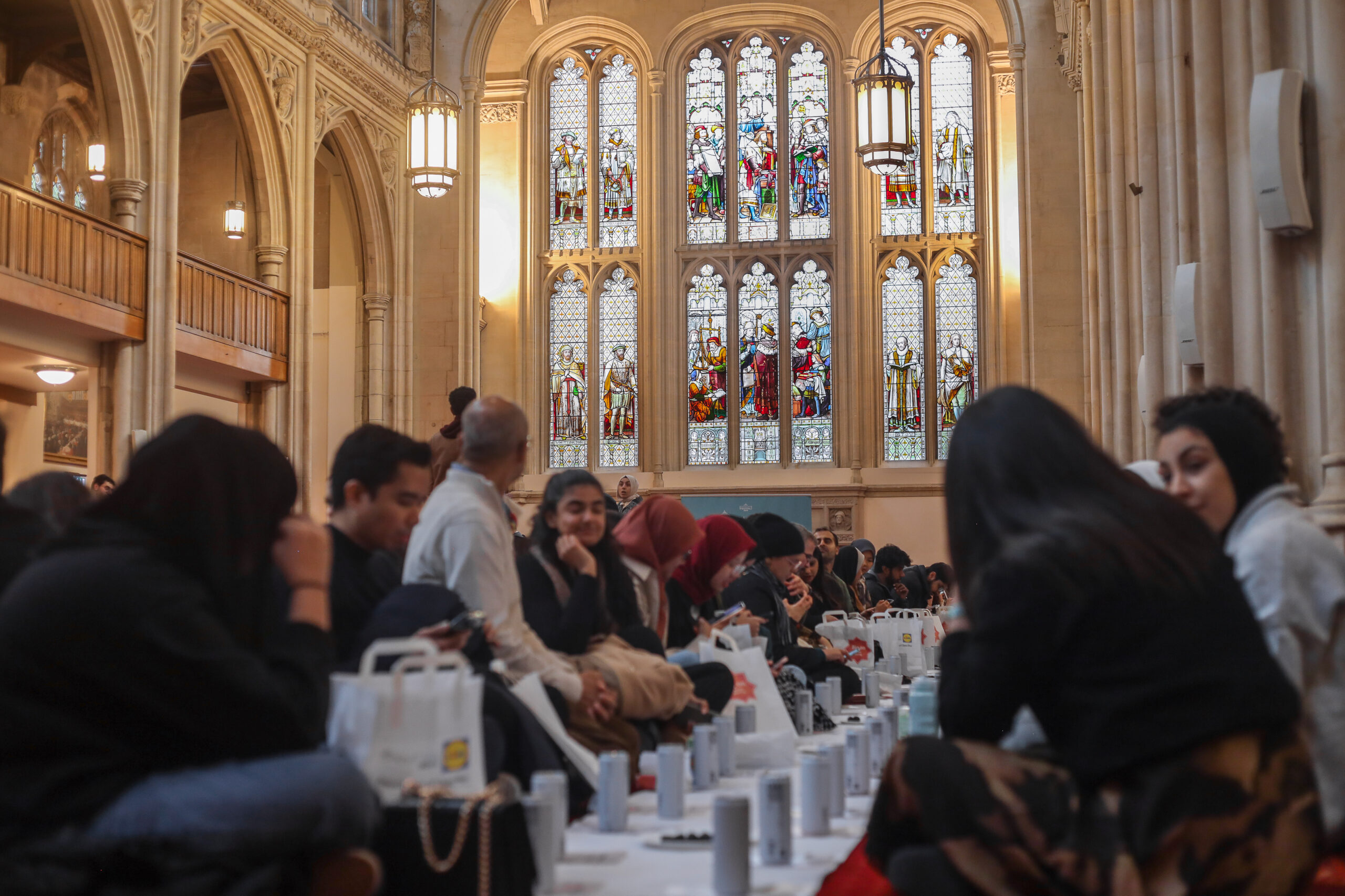 Open Iftar with people sitting in two lines on the floor and talking in Guildhall.