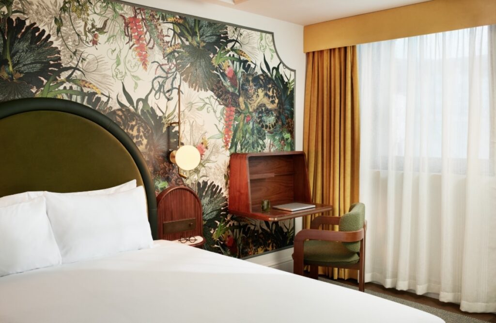 A close-up view of a bed adorned with white bedcovers against a backdrop of vibrant floral wallpaper.