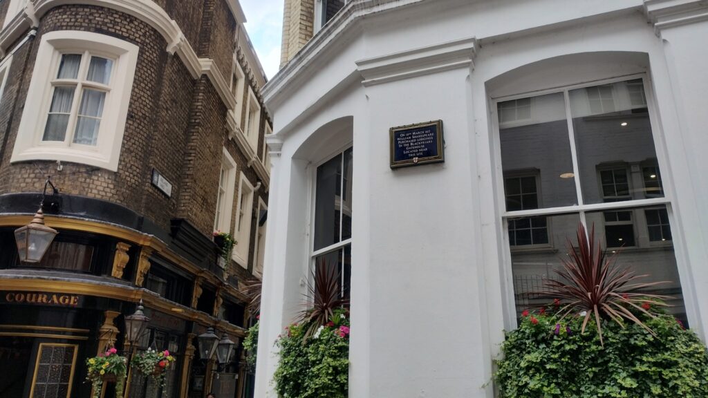 City of London Blue Plaque on a white building, opposite a historic pub.