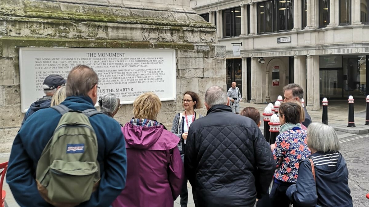 A group of people on a guided tour, listening to a guide in front of the Monument to the Great Fire of London.
