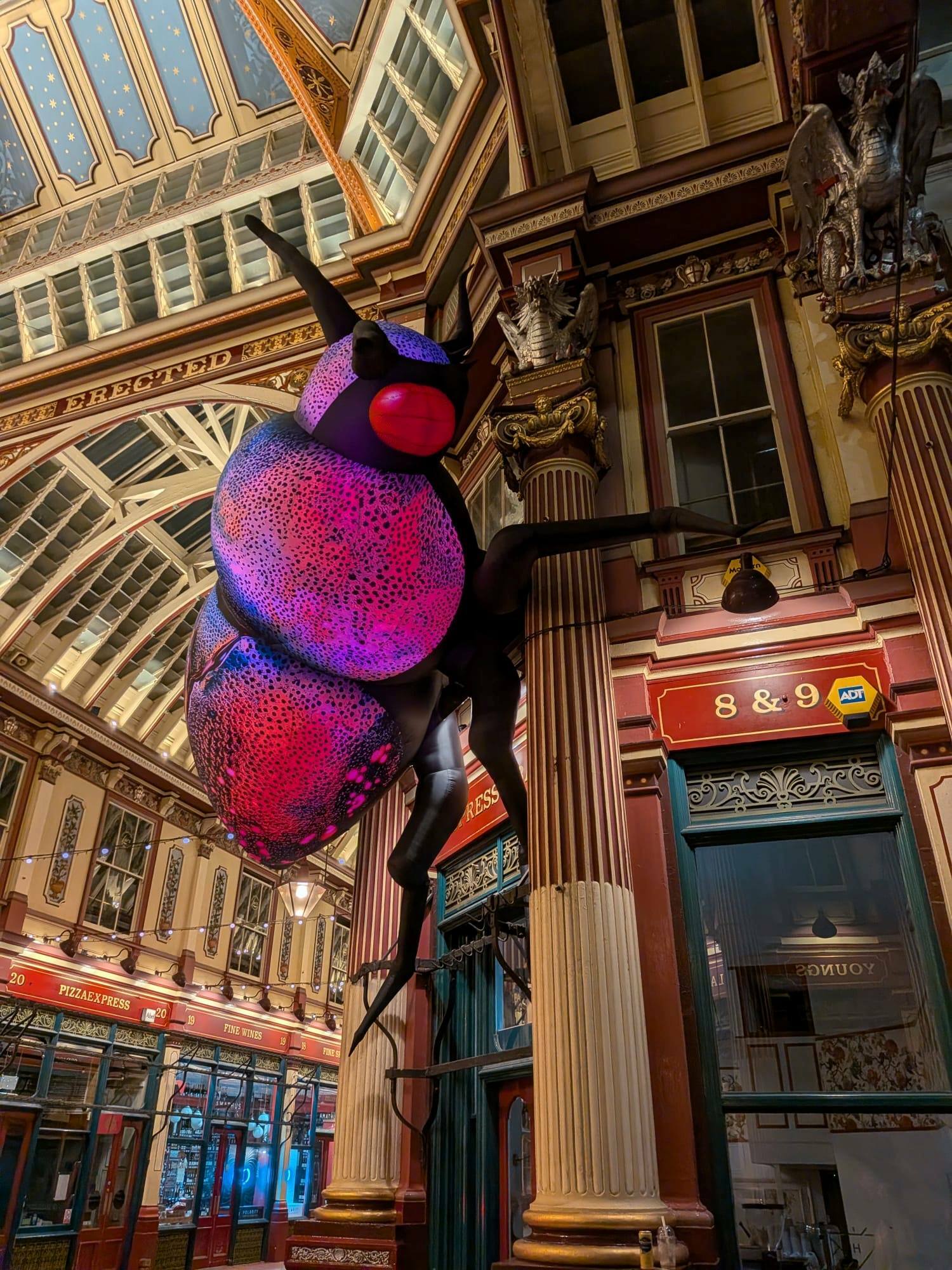 A giant jewel beetle in pink climbing the buildings of Leadenhall Market
