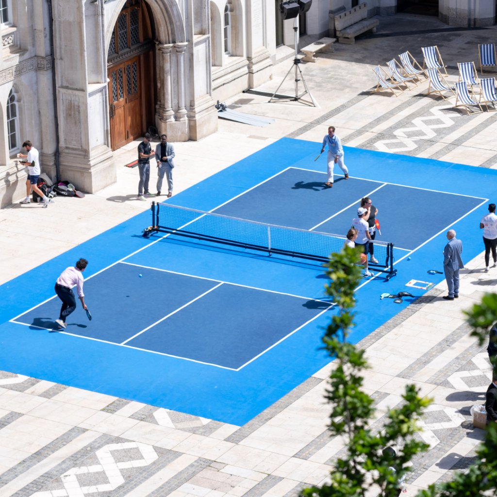 A blue padel court in the historic Guildhall Yard with people playing.