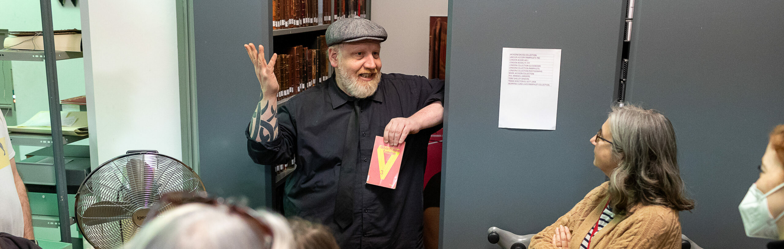 An individual presenting at a book event gestures animatedly to a group of attentive listeners in a bookstore.