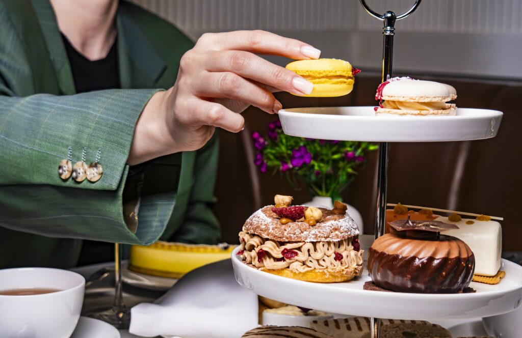 A person picking up a yellow macaroon off a cake tier during afternoon tea.
