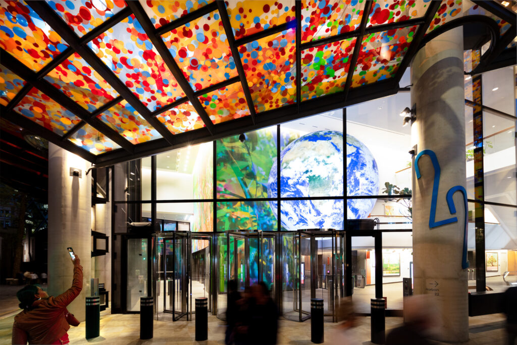 View of the entrance to 22 Bishopsgate, featuring a vibrant ceiling with colourful circles, a large globe display inside, and blurred figures of people entering and exiting the store.