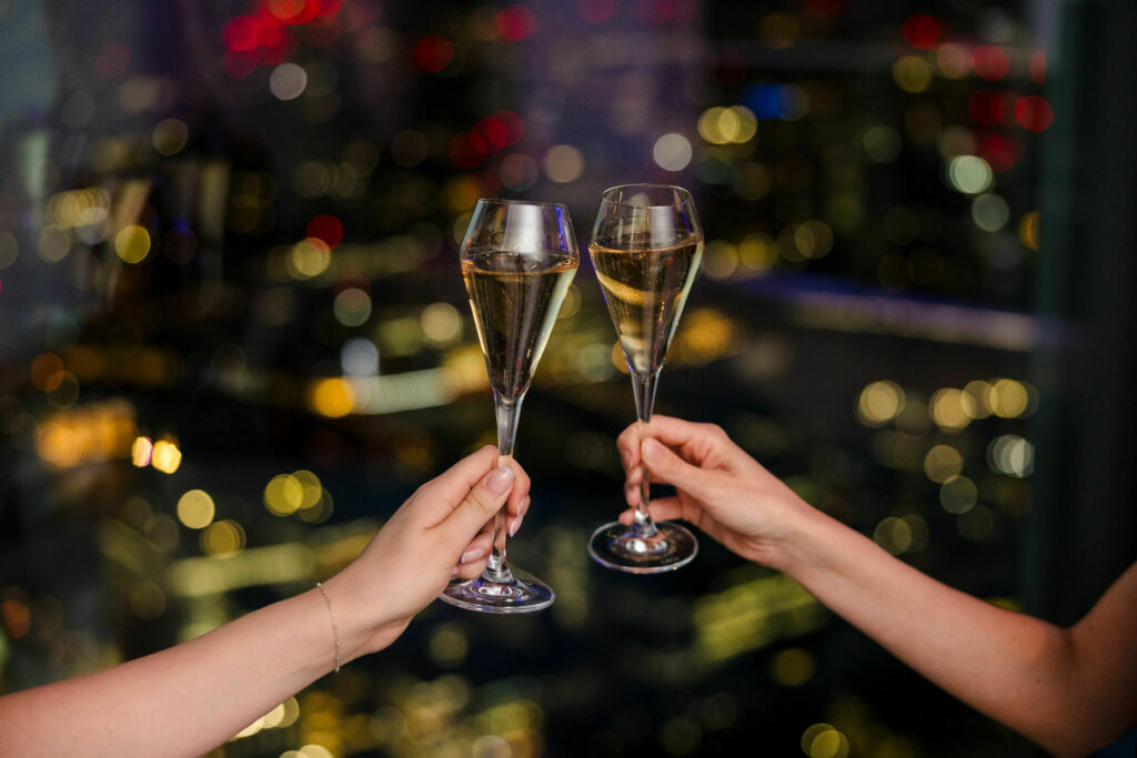 Two people toasting with champagne glasses against a blurry city lights background.