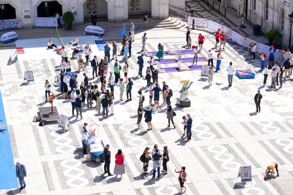 Aerial view of an outdoor event at Guildhall Yard with people engaging in various activities at booths and interactive displays under a clear sky.