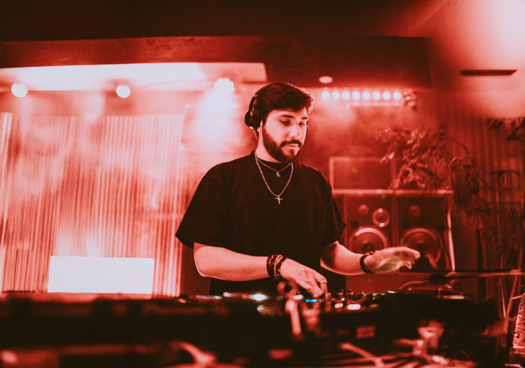 DJ performing at a mixing console under red stage lighting.