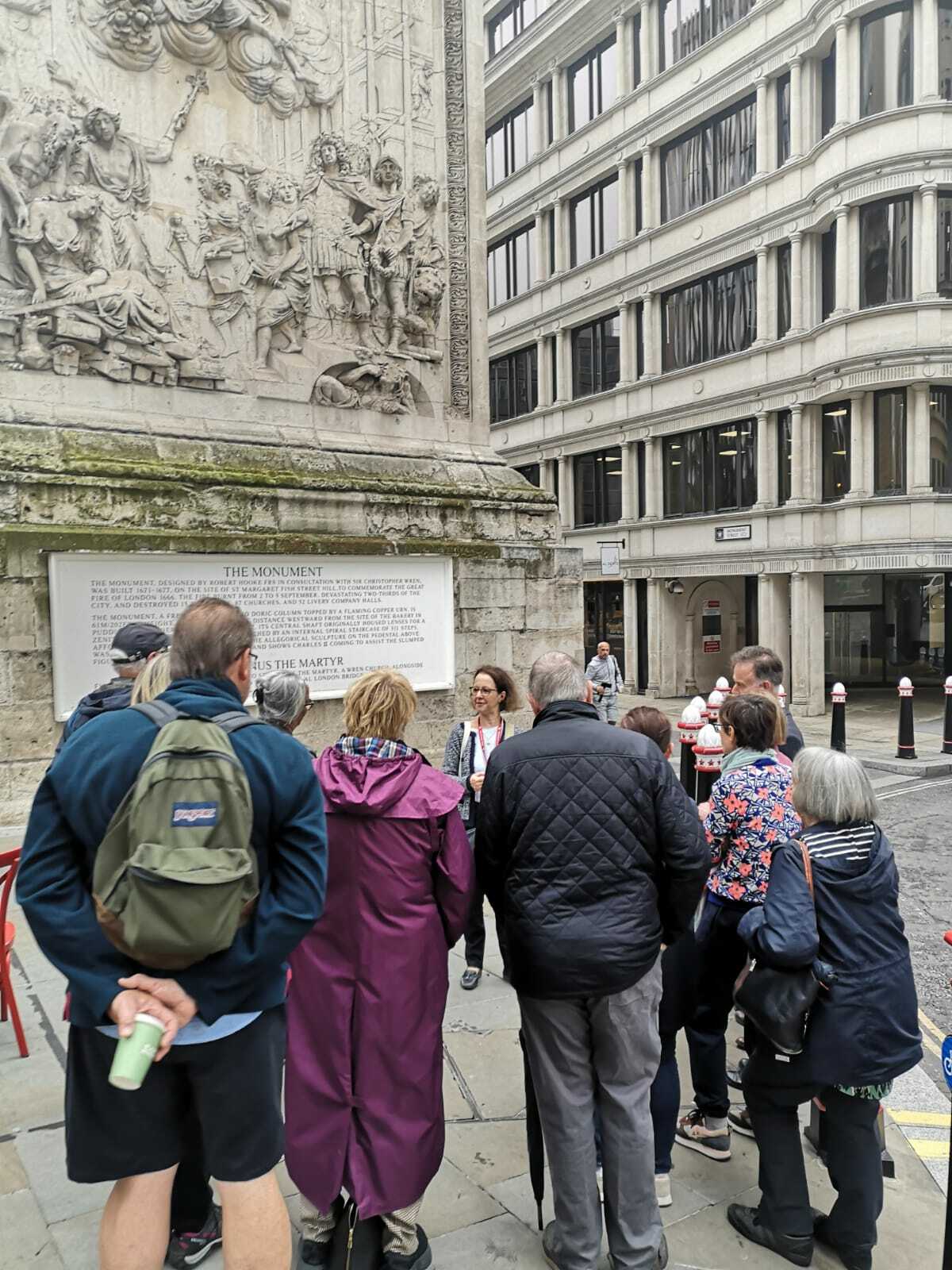 A group of people on a guided tour, listening to a guide in front of the Monument to the Great Fire of London.