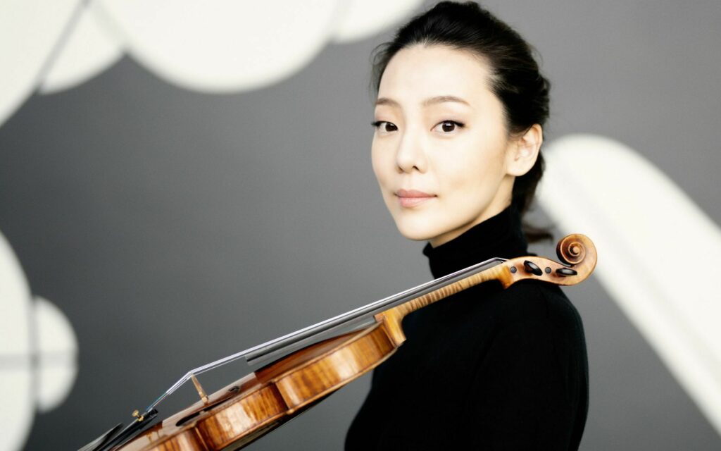Portrait of a violinist holding their instrument, with a softly blurred background of light circles.