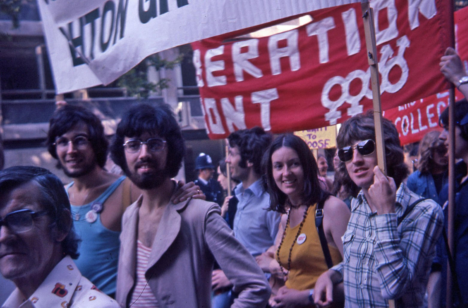 A group of individuals at a protest, holding signs that read "Action for Liberation" and "Vassar College." The atmosphere is lively, with people of various ages and expressions engaging actively with their surroundings.