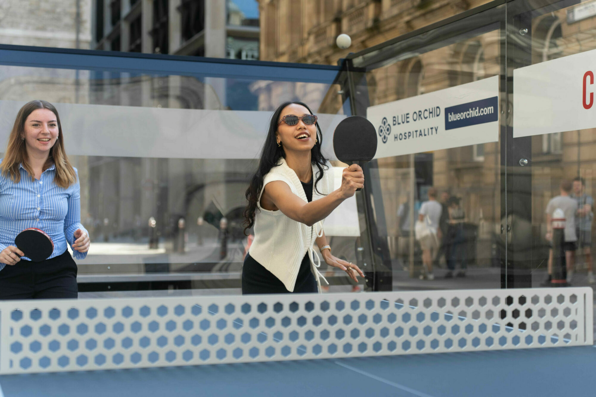 An image of two peolpe in a padel table tennis court, one is going to hit the incoming ball