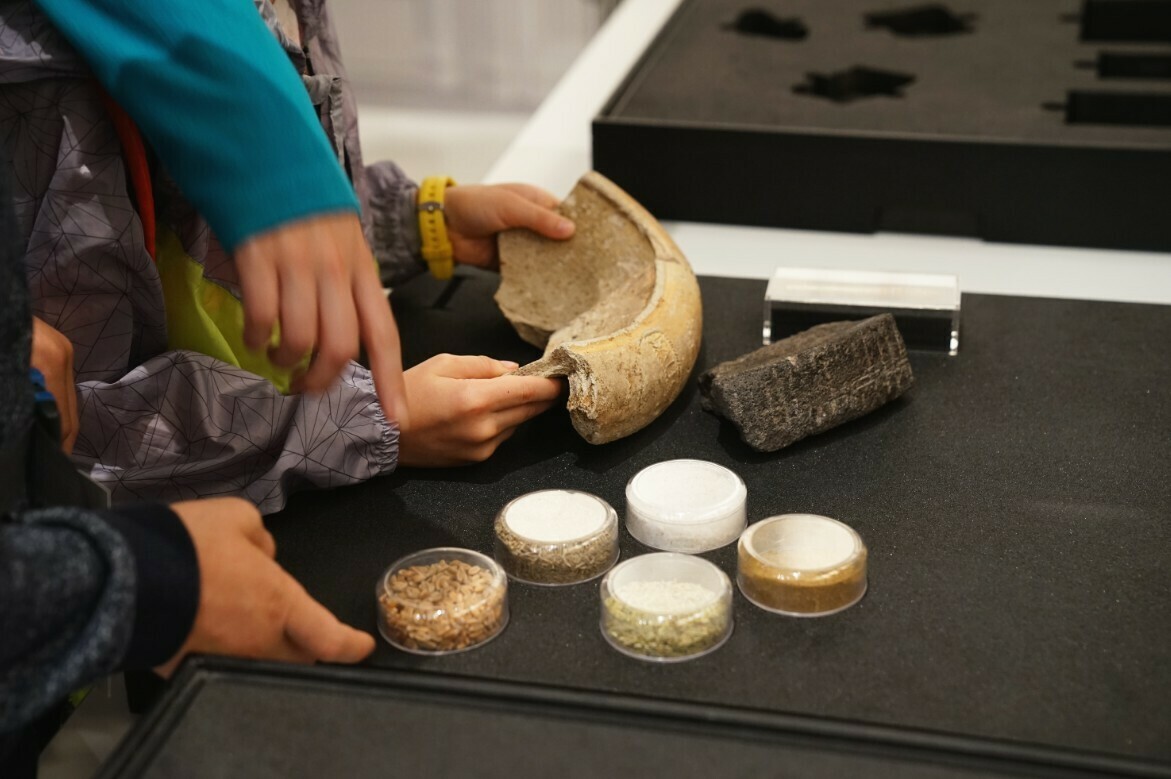 Image of two sets of hands examining a roman ceramic artefact.