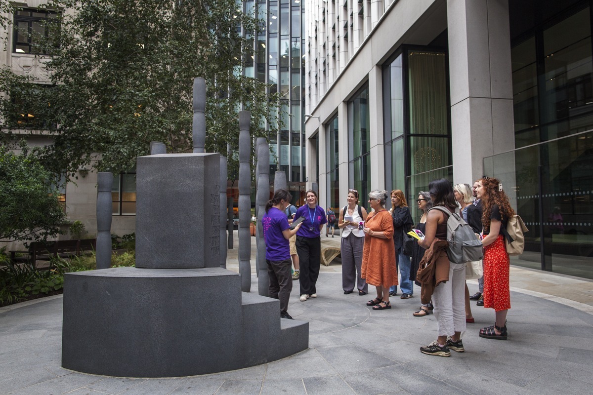 An image of a group of people stood around a large sculpture listening to a guide.