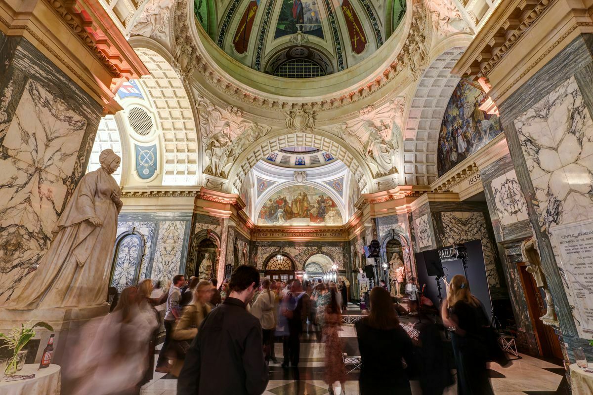A group of people attending a live music event inside a historic building, with statues, frescoes and marble decor