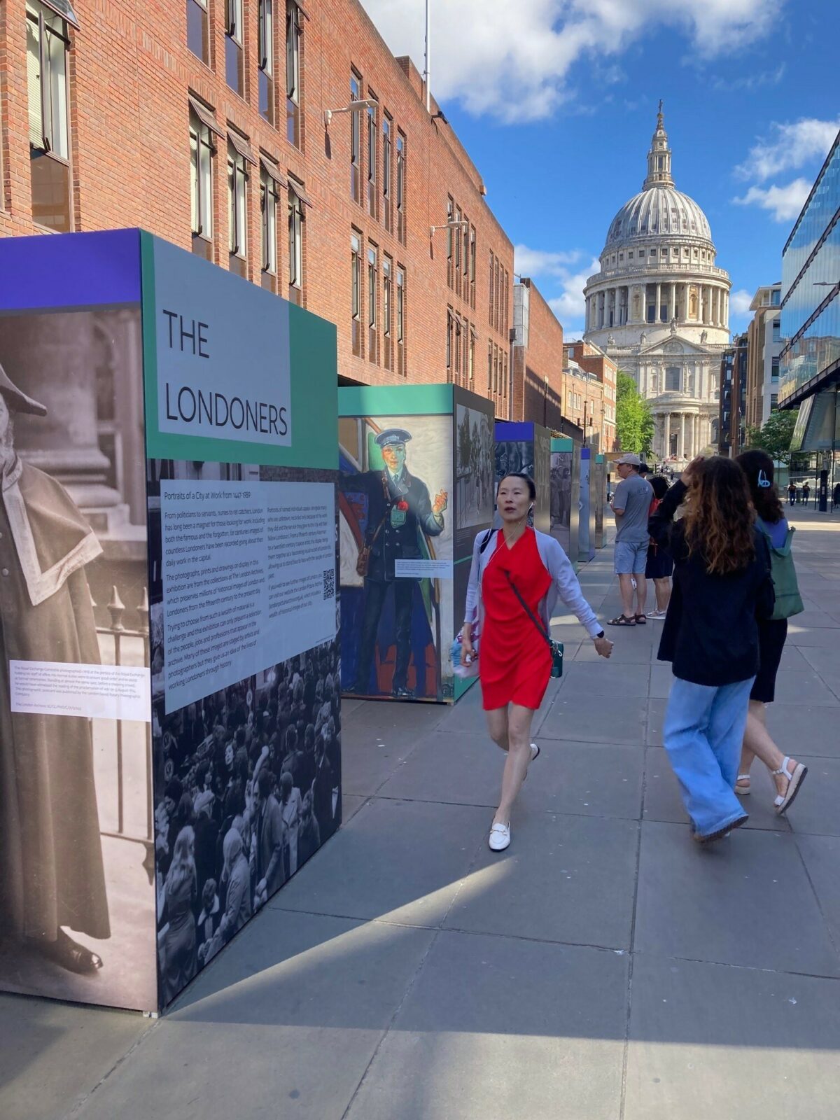 St Paul's is in the background with the London Archives exhibition in the foreground and people walking around it.