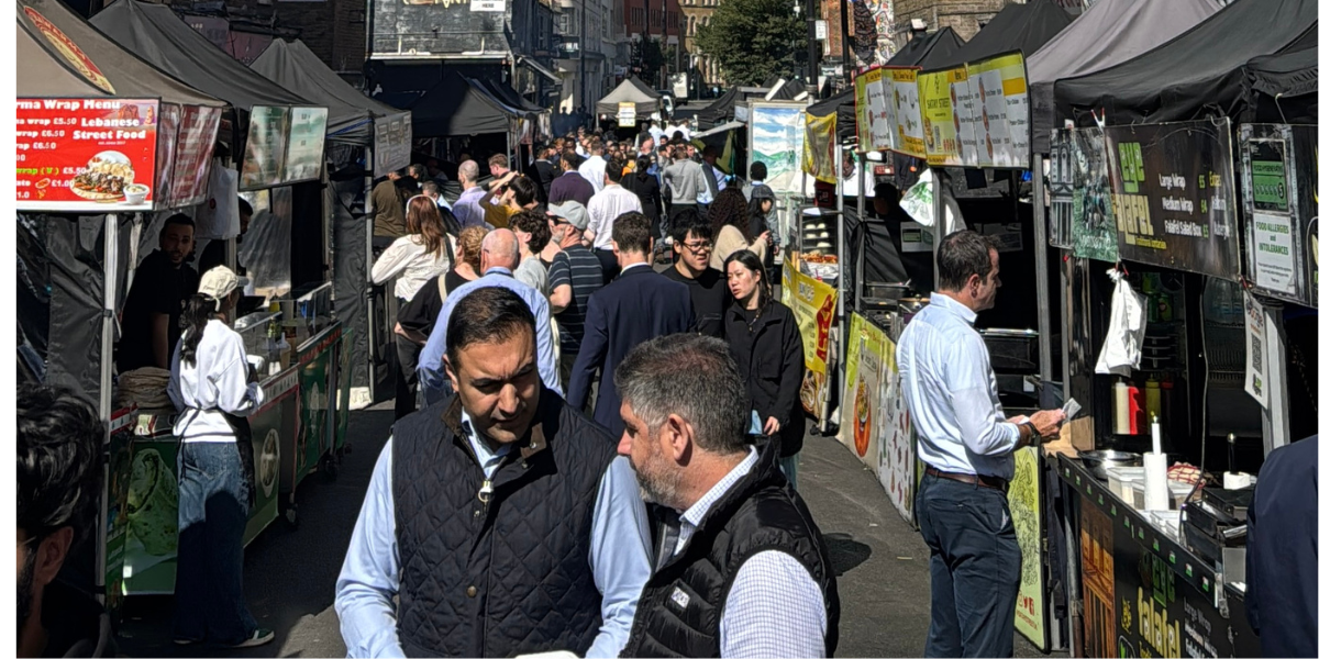 A crowd shot of lots of food stalls and people waiting in a food market
