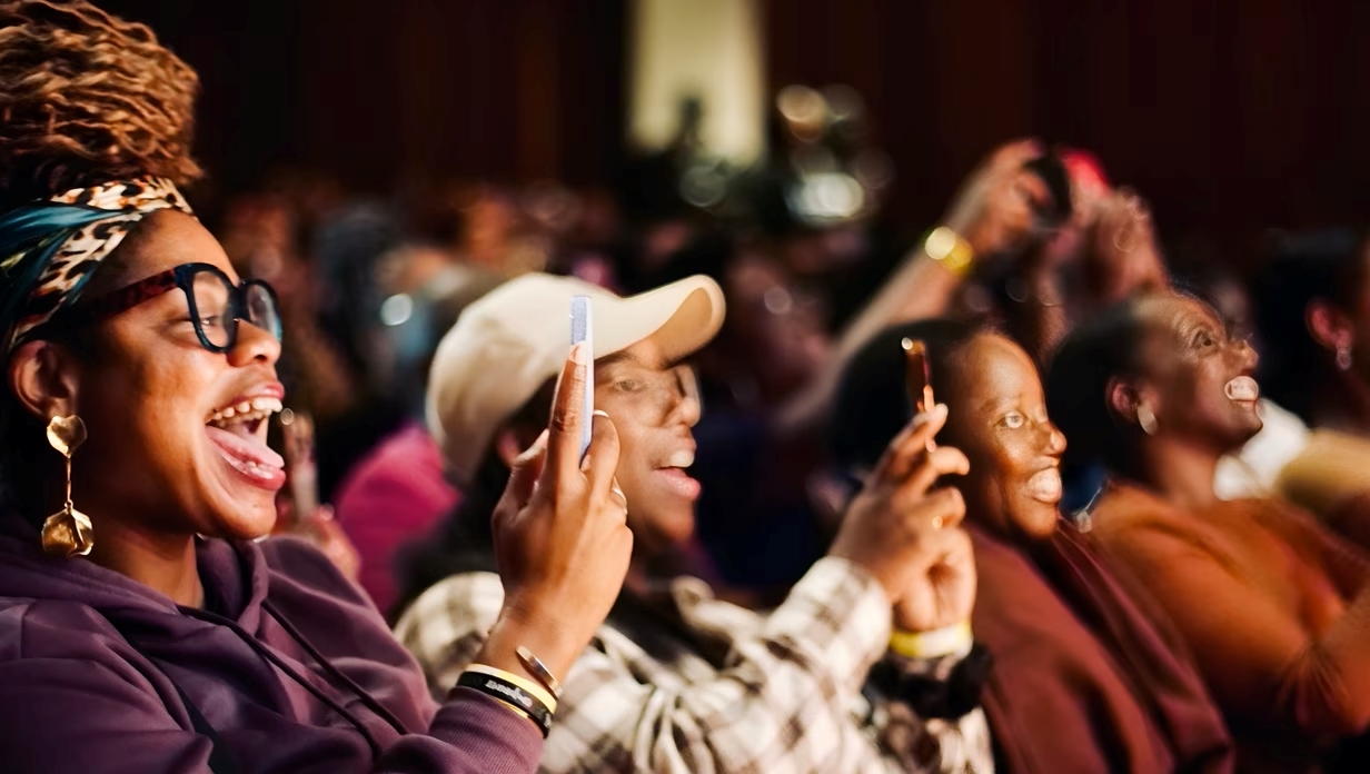 Various people smiling, some holding a phone up, it looks like they're watching something infront of them